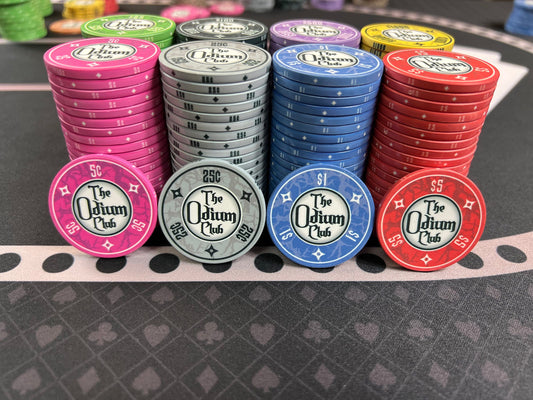 All eight of the stock colors and denominations of the modern-looking Odium Club poker chips in stacks of 20. Both faces are identical. Each side shows the logo and denom. Available in 5¢ pink, 25¢ gray, $1 blue, $5 red, $25 green, $100 black, $500 purple, and $1000 yellow. Shown up front: 5 cent pink, 25 cent gray, one dollar blue, and five dollar red.