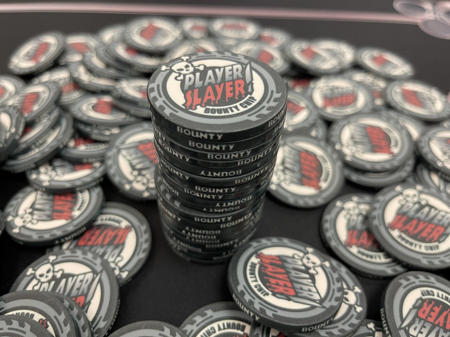A 20-chip stack of Player Slayer bounties, surrounded by a pot of black bounty chips. These masculine poker chips are designed to be a fun, easily recognizable addition to your bounty poker tournament. They even match most chips from other poker equipment shops.